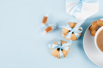 Cookies with cup of coffee on blue with gift in blue ribbon