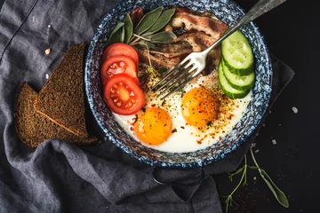 Photo sur Plexiglas Oeufs sur le plat Breakfast set. Pan of fried eggs with bacon, fresh tomato, cucumber, sage and bread on dark serving board over black background