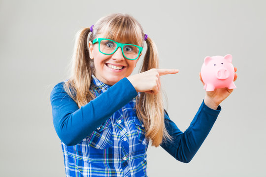 Studio shot portrait of happy nerdy woman who is pointing at piggy bank