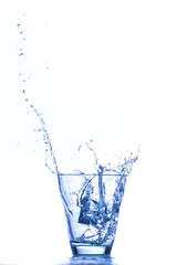 Bicchiere in vetro trasparente isolato su fondo bianco con schizzi e bollicine da   fuoriuscita d’acqua  