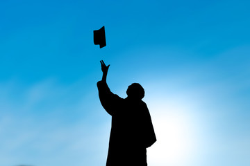 Graduates throwing hat on graduation day, silhouette