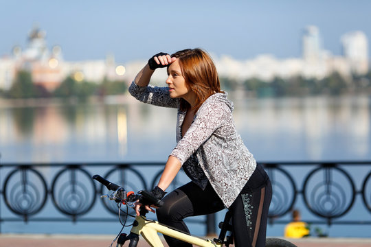 Young redhead woman riding a bike on embankment. Active people outdoors. Sport lifestyle.