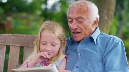  Grandfather & granddaughter sitting in the garden & reading together - Powered by Adobe