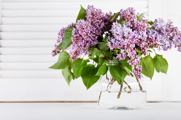 Blossom lilac flowers in glass vase on white shutters