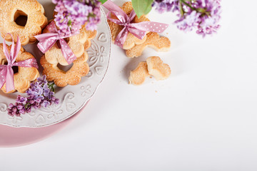 Fototapeta na wymiar Cookies with pink ribbon on white plate with lilac flowers from