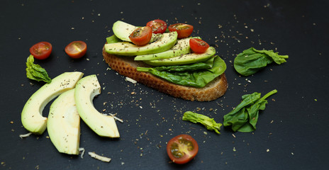 Close up of toast with spinach leaves, avocado and tomatoes.