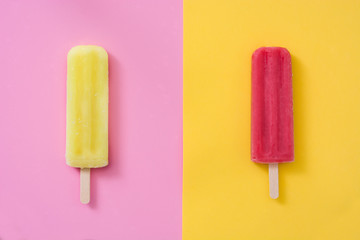 Red popsicle on yellow background and yellow popsicle on pink background
