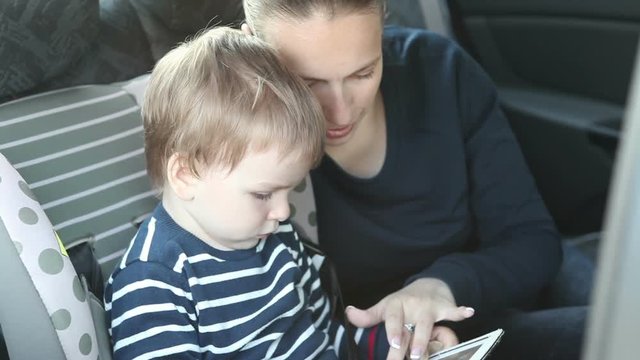Mom and young son using tablet sitting in the back seat of the car.