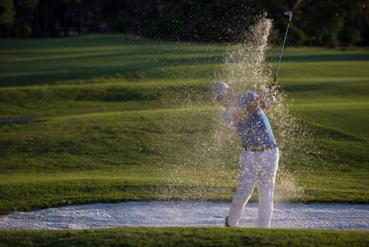 golfer hitting a sand bunker shot on sunset