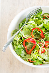 Frisch zubereiteter gemischter Salat in einem weißen Teller steht auf einem Holzbrett.