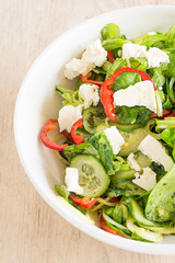 Frisch zubereiteter gemischter Salat mit Fettkäse in einem weißen Teller.