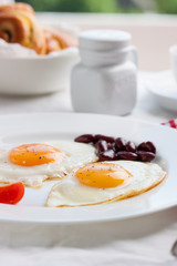 Homemade fried eggs with tomatoes and red kidney beans on a plate on a table with kitchen background, closeup