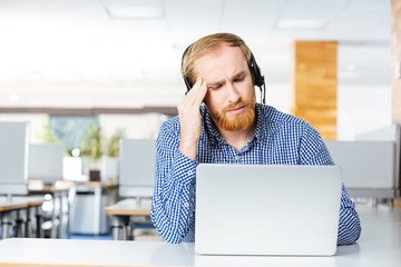 Man with headset and laptop suffering from headache on workplace