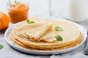 Thin crepes or pancakes with butter, honey and sour cream on a rustic textile background
