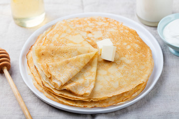 Thin crepes or pancakes with butter, honey and sour cream on a rustic textile background