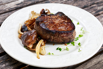 Tasty Beef Mignon steak with mushrooms and herbs on plate.