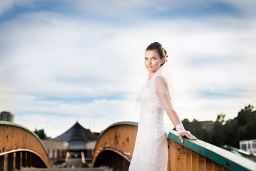 Beautiful brunette bride posing on the bridge in park