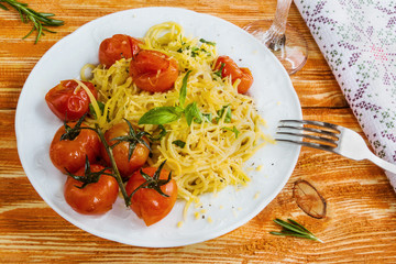 Pasta with small cherry tomatoes baked with garlic, salt and olive oil. White plate on wooden background.
