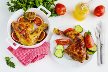 Roasted chicken legs, red oranges, garlic and parsley in white baking dish and on white plate on white table. Cooked with sauce from orange, honey and olive oil. Top view.