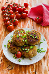 Roasted chicken cutlets with green onion on white plate and small cherry tomatoes on wooden background.