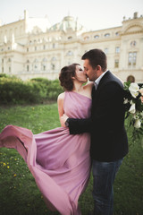 Naklejka premium Wedding. Couple. Krakow. The bride in a pink dress and groom posing on background of theater