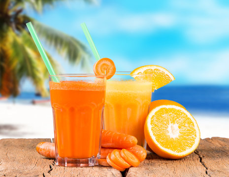Fresh juice orange and carrot on wood with tropical beach background