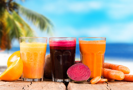Fresh juice orange, beetroot and carrot on wood with tropical beach background