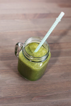 A green smoothee in a mason jar with tube on wooden background