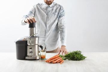 Focused on carrots. Unrecognizable man presses carrots inside metallic professional juicer to make...