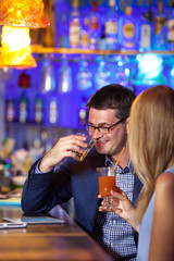 Handsome man enjoying drinks with a female companion in a brightly colored nightclub interior seated at a table together