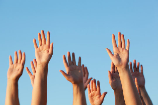 Group of people raising their hands in the air against a clear sunny blue sky in a conceptual image with copy space