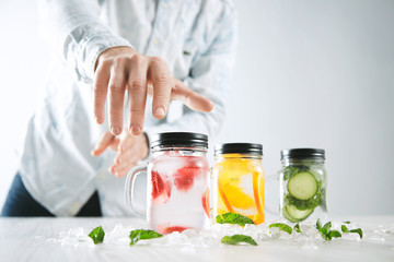 Hand takes one of rustic jars with cold fresh homemade lemonades from strawberry, orange, cucumber, ice and mint Close focus on first jar, action move, summer mood