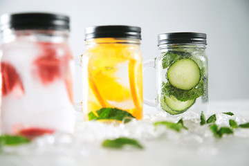 Fototapeta na wymiar Close focus on last jar Healthy fresh cool homemade lemonades with sparkling water strawberry, cucumber,mint and orange isolated in smashed ice cubes on wooden table