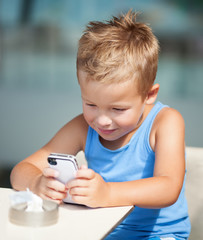 Adorable smiling blond boy using cell phone