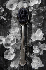 Vintage silver aged brushed teaspoon with black caviar isolated on black marble desk surrounded...