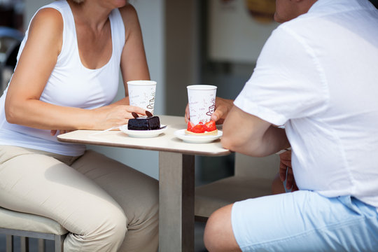 Close Up of Couple Seated Opposite Each Other and Enjoying Coffee and Cake Desserts Together on Sunny Outdoor Cafe Patio