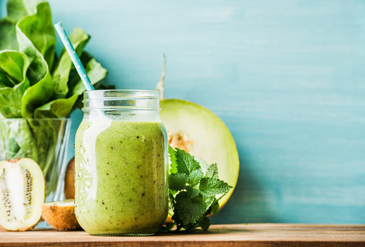 Freshly blended green fruit smoothie in glass jar with straw