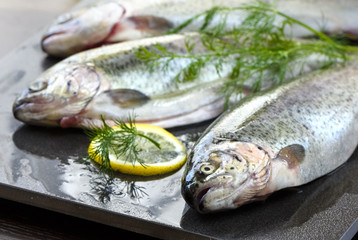 Raw rainbow trouts on a stone board, with herbs and lemon, ready for cooking