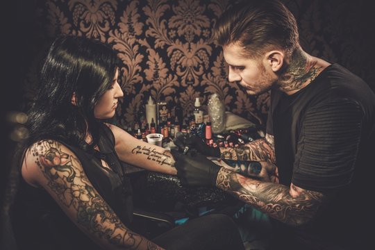 Naklejki Professional tattoo artist makes a tattoo on a young girl's hand.