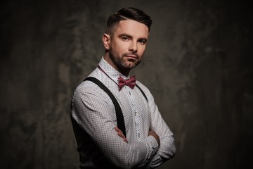 Stylish man with bow tie wearing suspenders and posing on dark background.