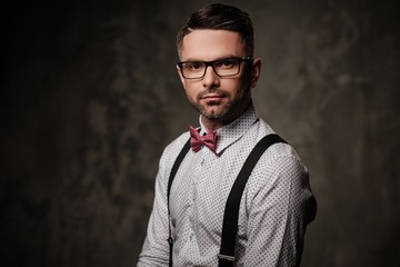 Fototapeta na wymiar Stylish man with bow tie wearing suspenders and posing on dark background.