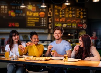 Cheerful multiracial friends having fun eating in pizzeria.