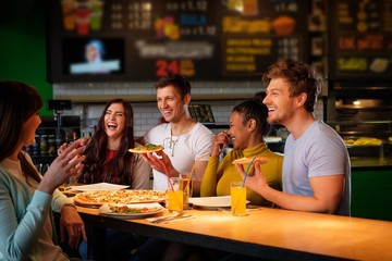 Cheerful multiracial friends having fun eating pizza in pizzeria.