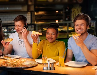 Cheerful multiracial friends having fun eating pizza in pizzeria.