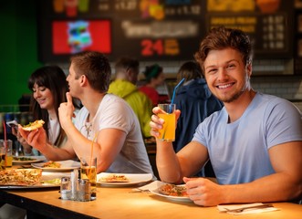 Cheerful multiracial friends having fun eating pizza in pizzeria.
