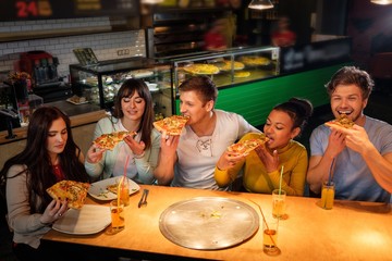 Cheerful multiracial friends having fun eating pizza in pizzeria.