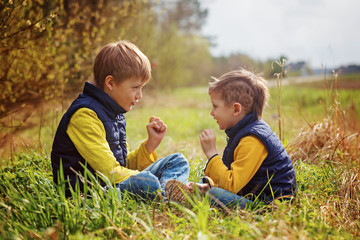 Naklejka na ściany i meble Two little brothers play in rock-paper-scissors sitting on grass