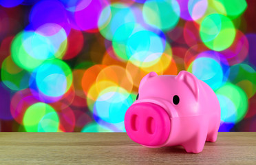 Pink piggy bank on wooden table with colorful blurred bokeh background.