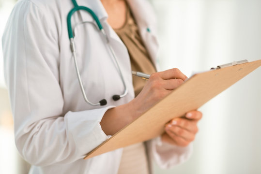Closeup on female doctor writing in clipboard