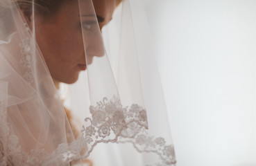 Portrait of beautiful bride with fashion veil posing at home at wedding morning. Makeup. Blondegirl with elegant hair styling. Wedding dress. Close Up